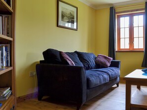 A living room with a dark sofa, a wooden table, a bookshelf, and a framed picture on the wall. - 2 bedroom accommodation in Dornie (Dornie)