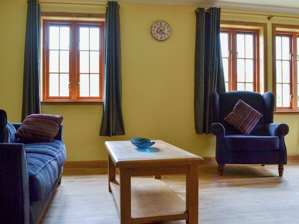 A room with a sofa, armchair, wooden table, and a wall clock.