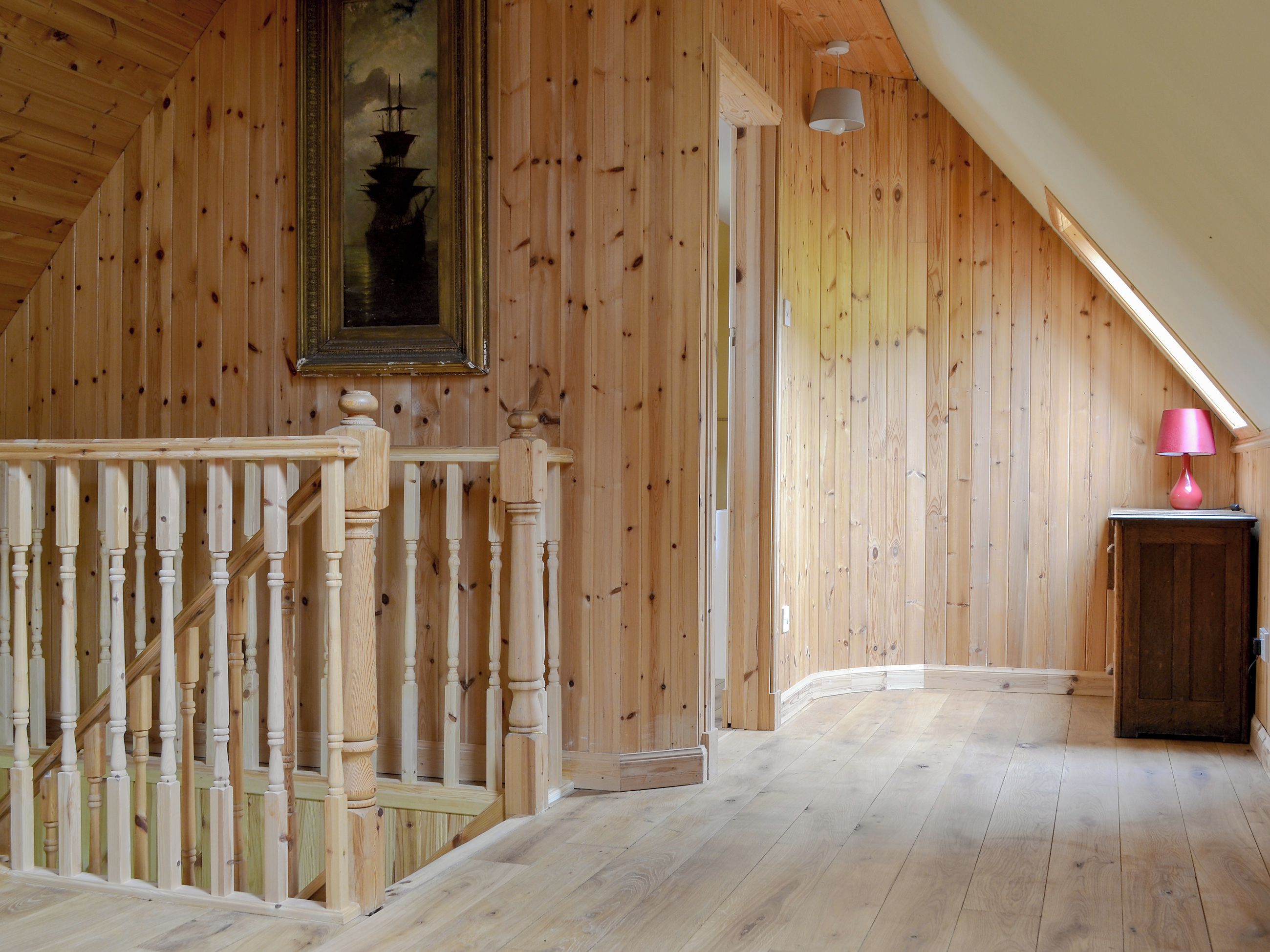 A wooden interior with a staircase, a painting, and a lamp.