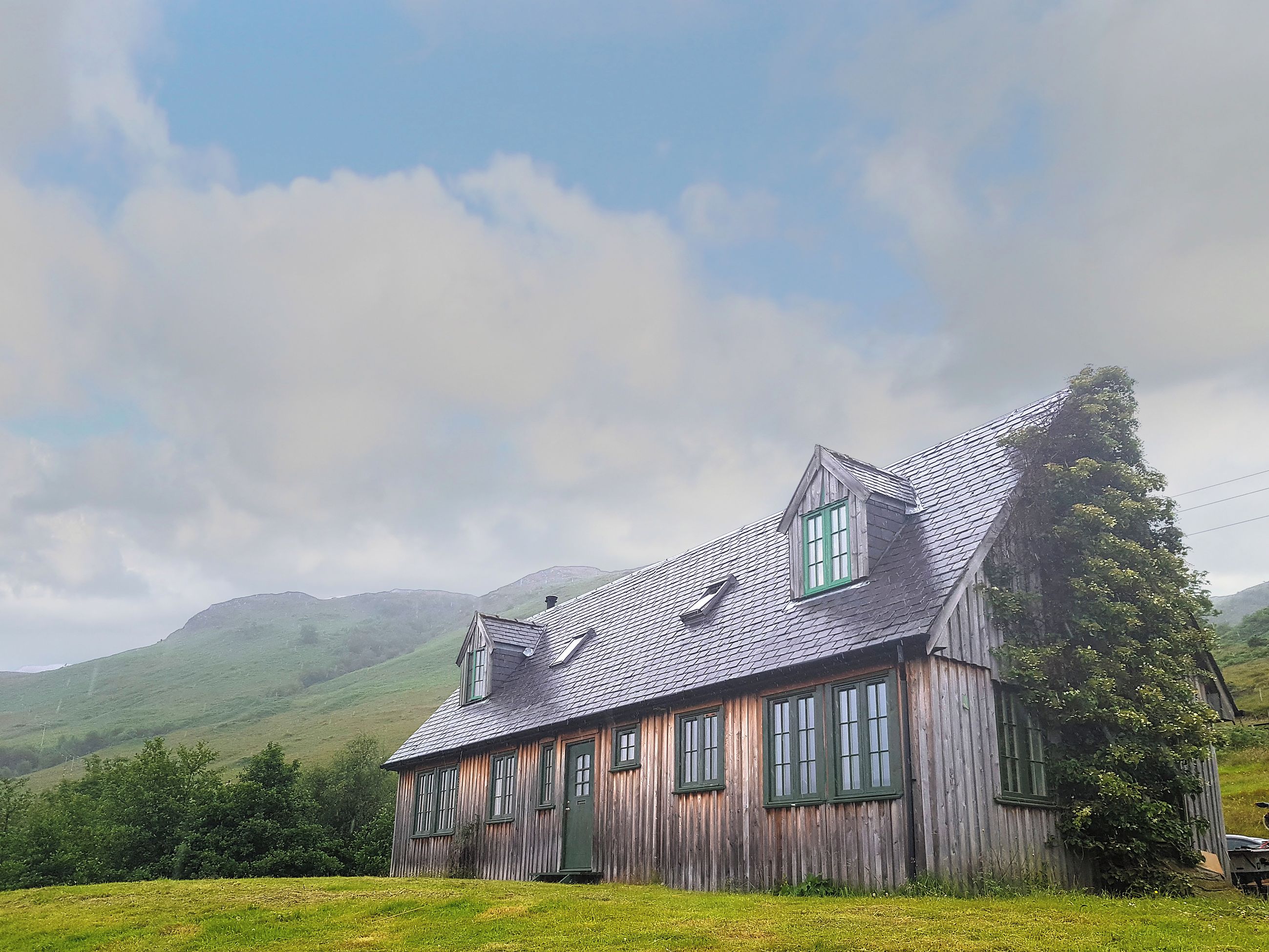 A wooden house with a steeply pitched roof, multiple windows, and a door.