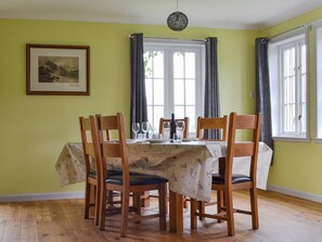 A dining room with a table set for six, wooden chairs, a framed picture on the wall, and a window with curtains.