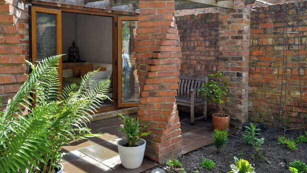 A brick house with a glass door leading to a living area, a wooden bench, and potted plants. - 2 bedroom accommodation in York (York)