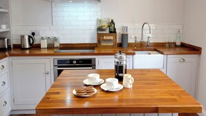 A kitchen with white cabinets, a wooden countertop, a coffee maker, and a breakfast setup with cookies and cups. - 2 bedroom accommodation in York (York)