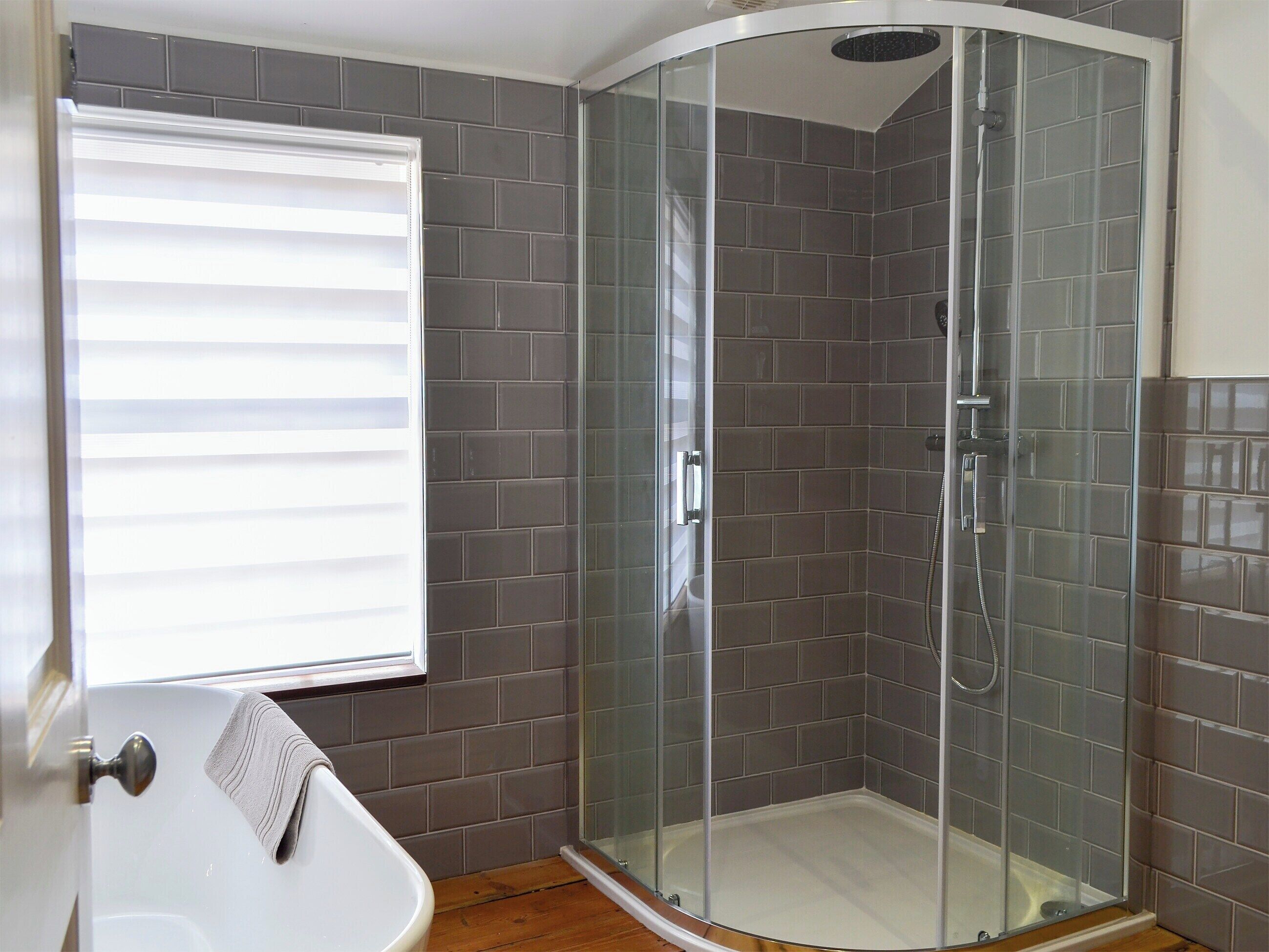 A corner shower with glass doors and a white bathtub with a towel hanging on the wall.