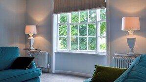 A room with a large window, two lamps, a radiator, and a teal sofa with a green pillow. - 2 bedroom accommodation in York (York)