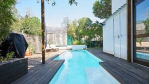 A rectangular swimming pool with a wooden deck surrounding it, a covered grill, and a white outdoor seating area. - Central Holiday Home Pool by Portugal Portfolio (Cascais)