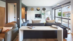 A modern living room with a sofa, a coffee table, and a TV. There are decorative plates on the wall and a window with a view outside. - Central Holiday Home Pool by Portugal Portfolio (Cascais)