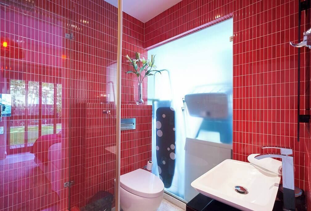 Un baño con paredes de azulejos rojos, un inodoro blanco y un lavabo.