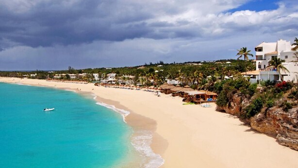 Una playa con agua turquesa cristalina, orilla de arena y edificios con balcones con vistas a la playa.