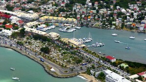 Vista aérea de un pueblo costero con un puerto deportivo, edificios residenciales y una carretera que lleva al agua.