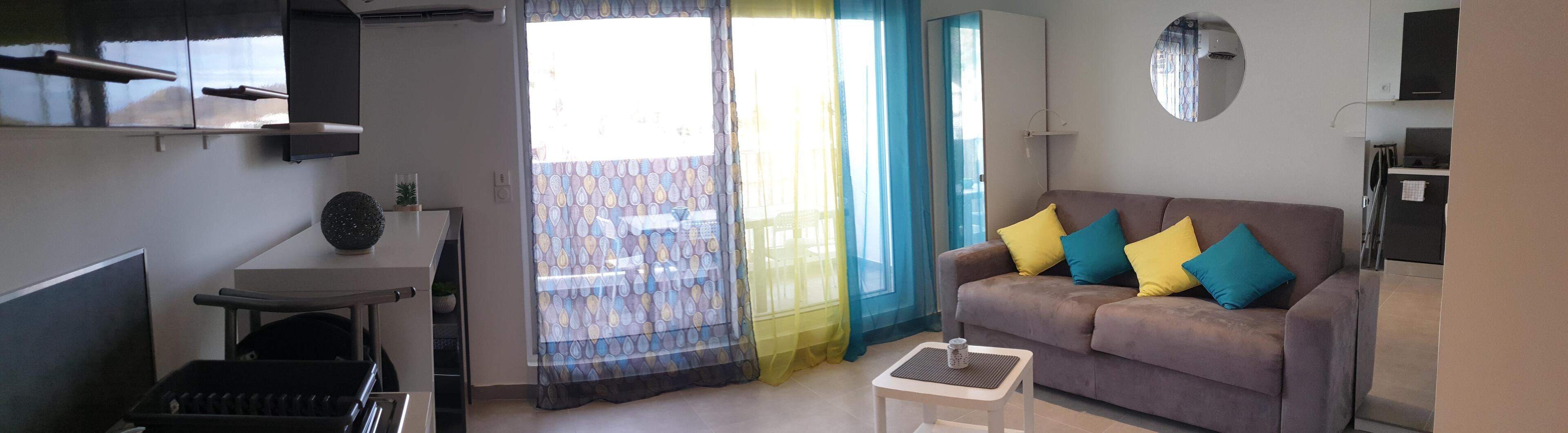 A compact living space with a sofa, a small table, a chair, and a kitchenette area.