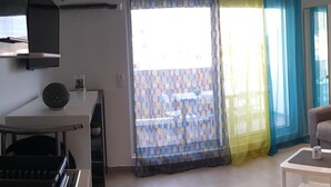 Un espacio habitable pequeño con un sofá, una mesita, una silla y una zona de kitchenette.