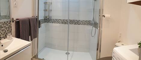 Une salle de bain moderne avec une douche à parois de verre, des toilettes et un lave-linge.
