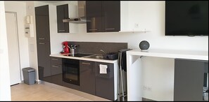 Une cuisine compacte avec des meubles de couleur sombre, un four encastré, un évier et une machine à café.