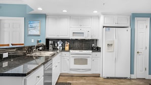 Una cocina moderna con armarios blancos, encimera negra, microondas, horno y refrigerador.