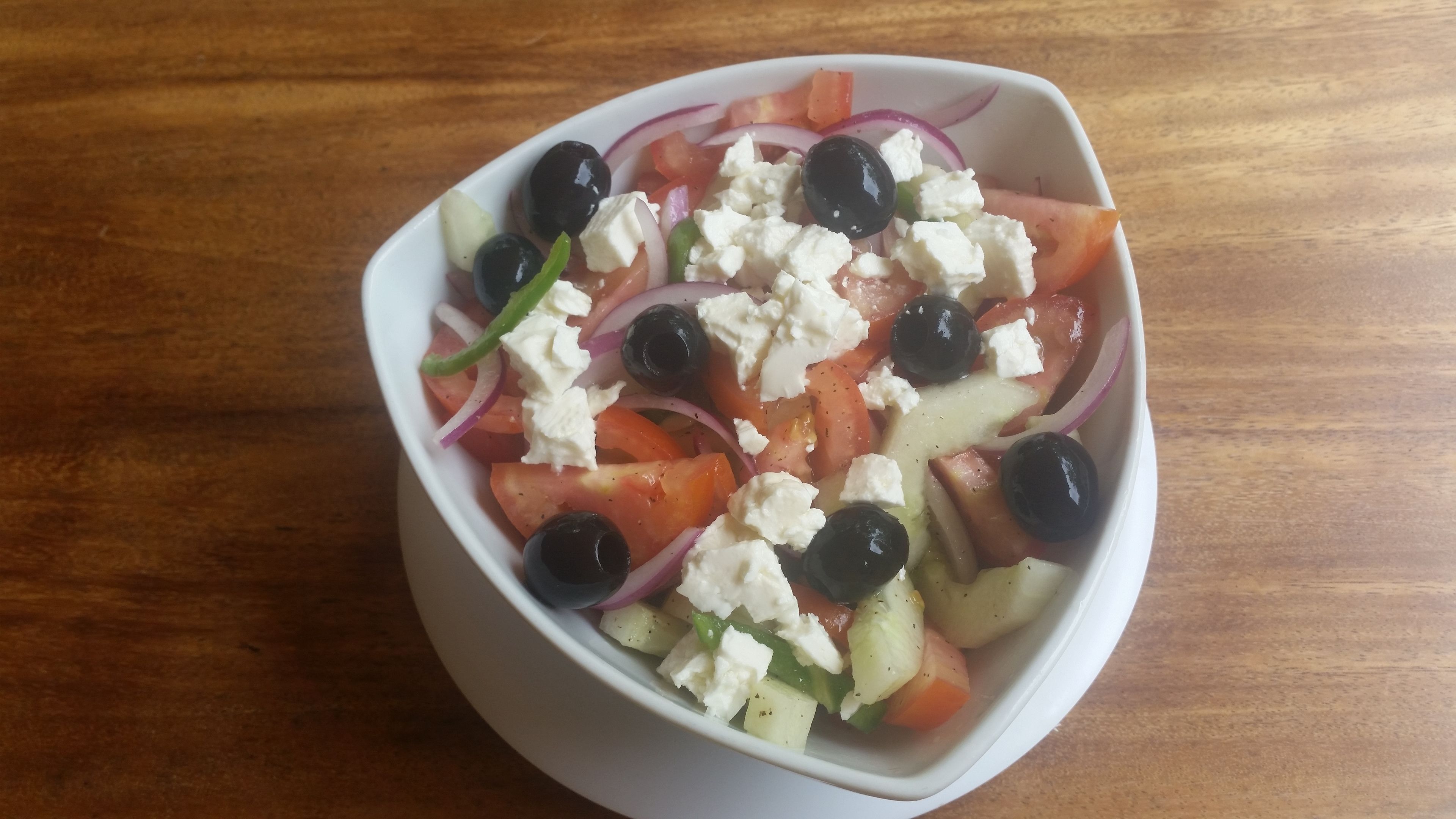 Ensalada con tomates, pepinos, cebollas moradas, aceitunas negras y queso feta sobre una mesa de madera.
