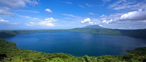 A panoramic view of a lake surrounded by lush greenery and mountains under a clear sky.