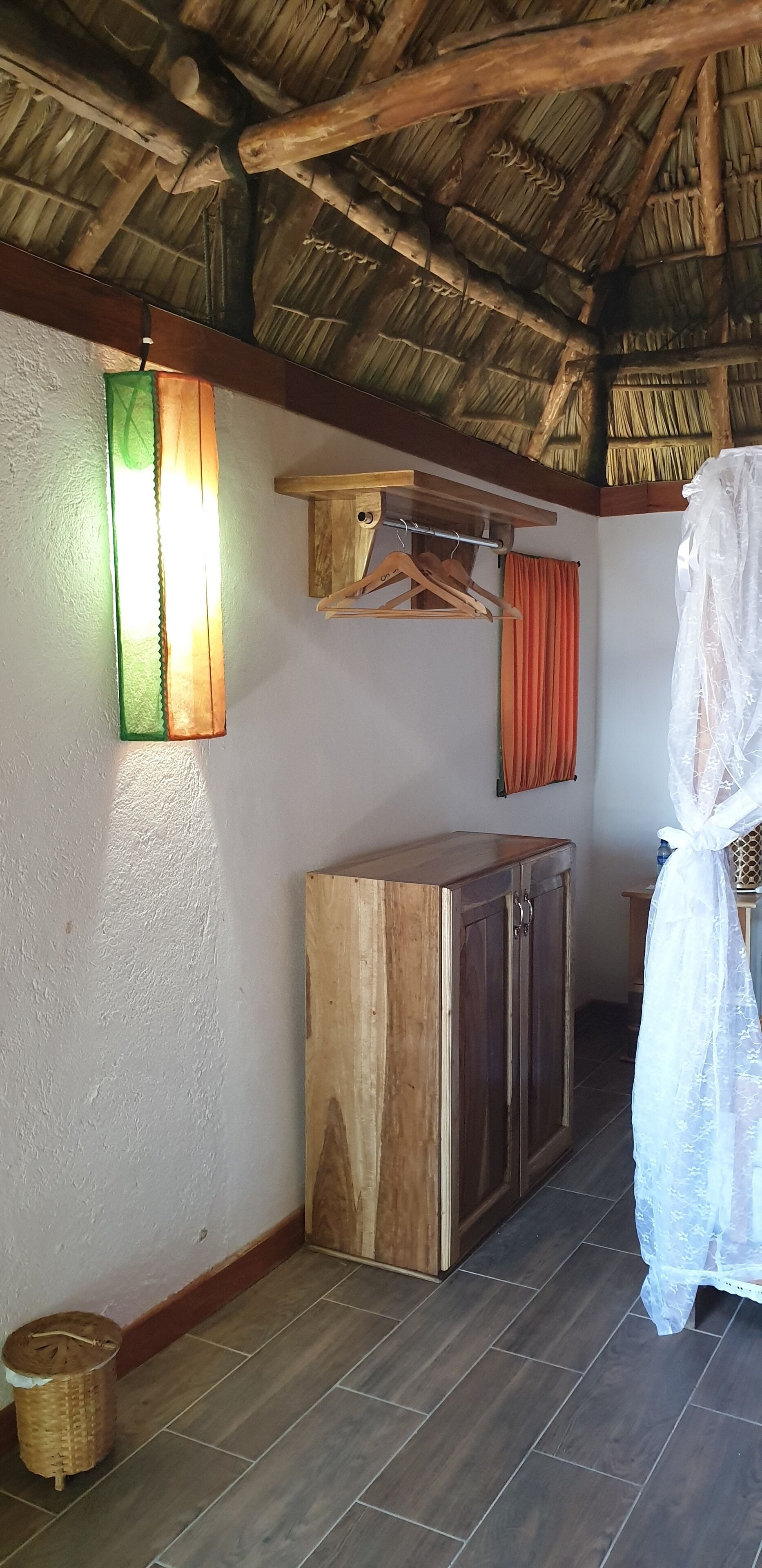 A room with a wooden cabinet, a hanging light fixture, a wooden shelf, a red curtain, and a wicker basket.
