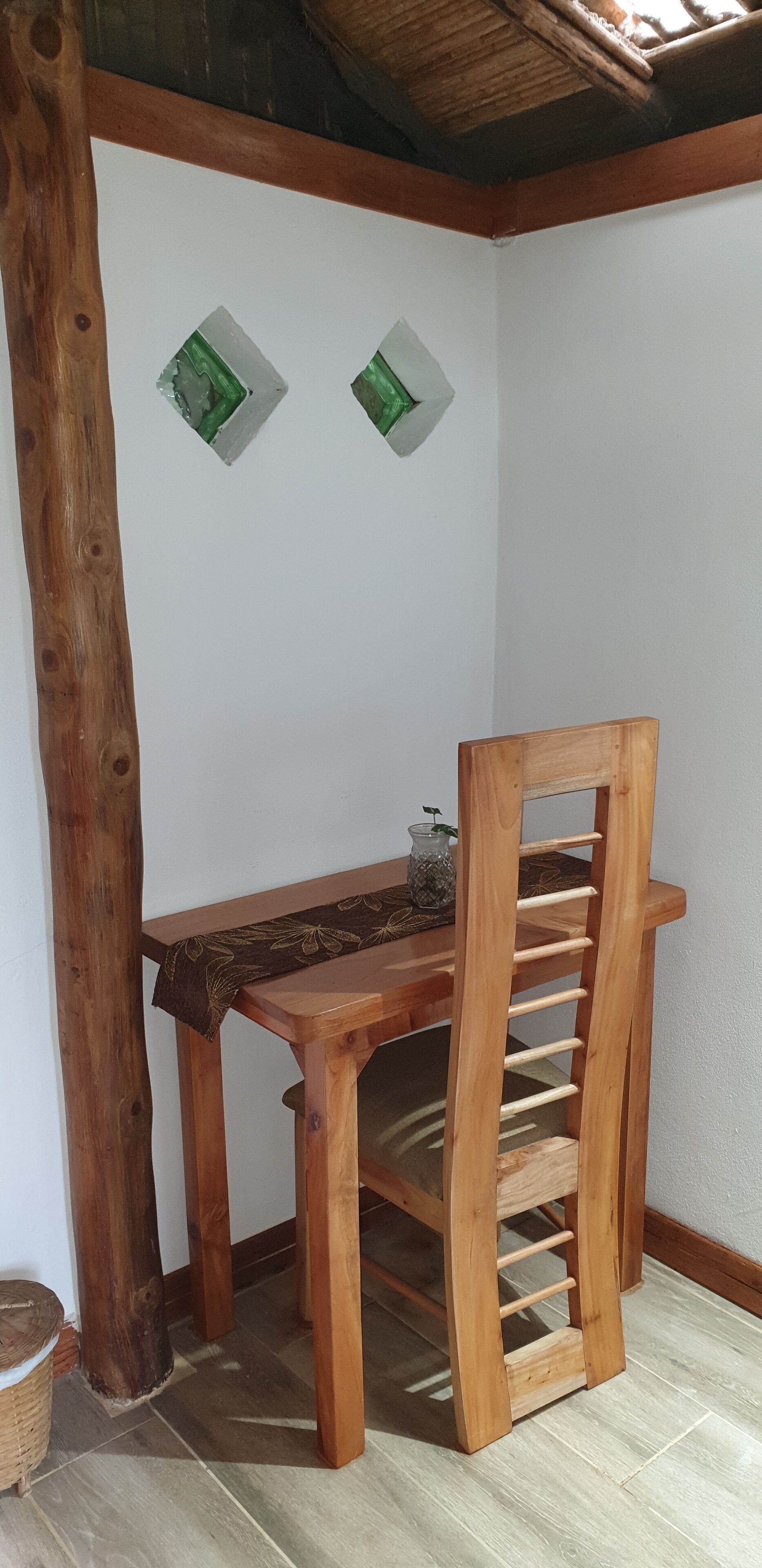 Una mesa de madera con una silla en un rincón de una habitación con paredes blancas y techo de madera.