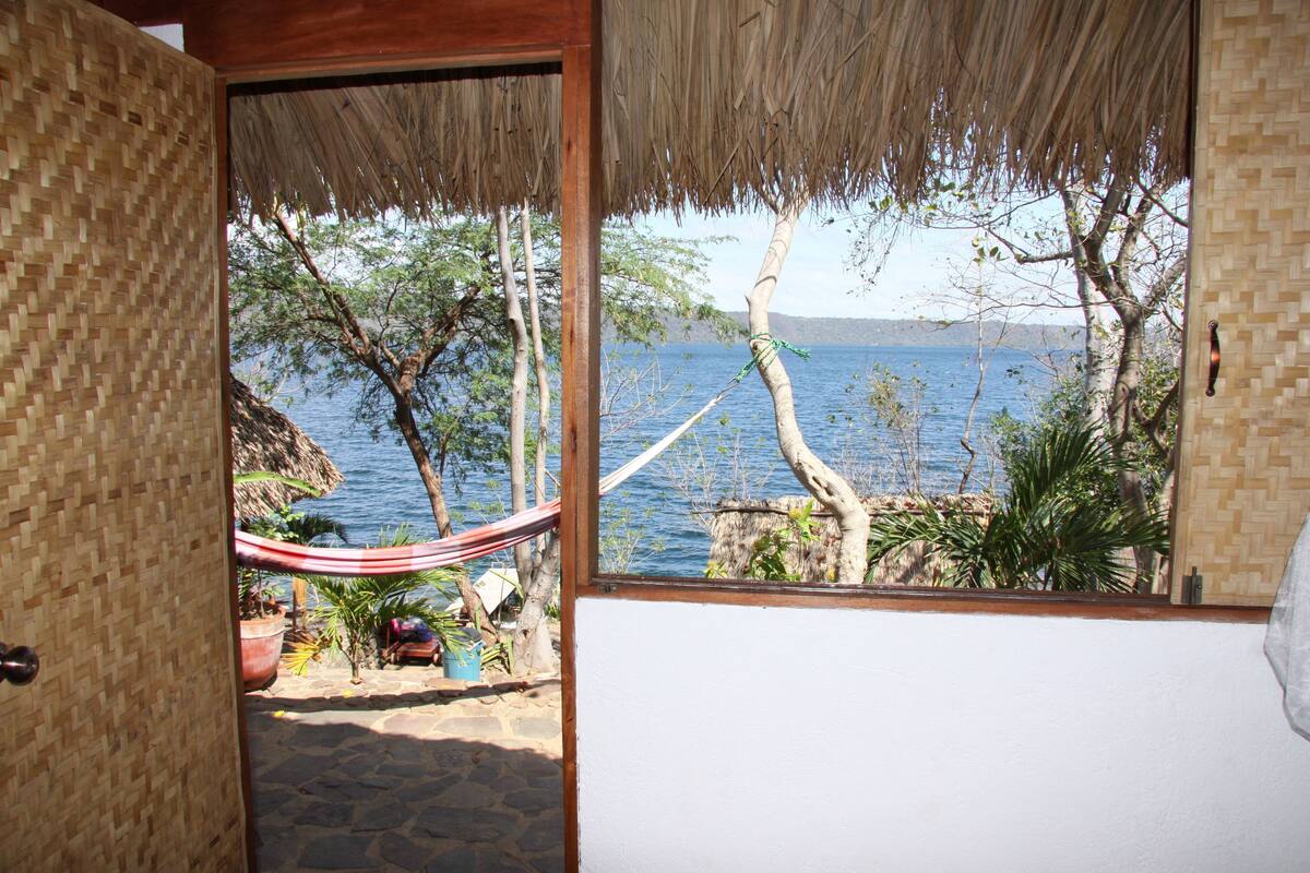 A room with a view of a lake, a hammock, and potted plants.