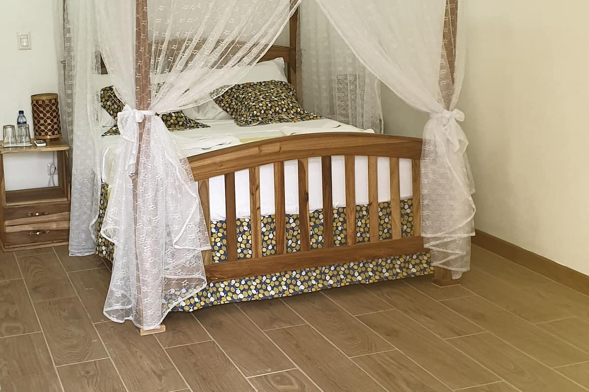 A bedroom with a wooden bed, a canopy, a ceiling fan, and a nightstand with a water bottle.