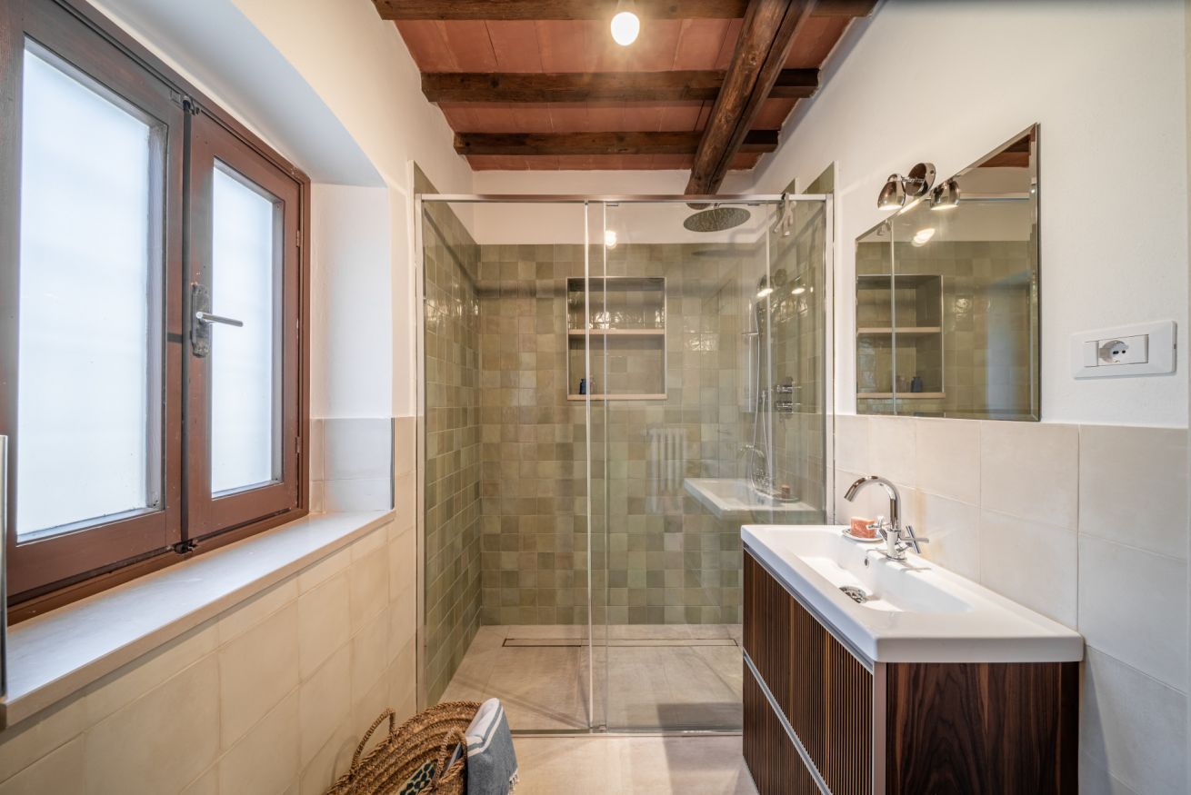 A bathroom with a glass shower enclosure, a wooden vanity, and a window with frosted glass.
