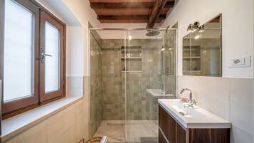 A bathroom with a glass shower enclosure, a wooden vanity, and a window with frosted glass.