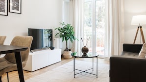 A modern living room with a sofa, a dining table, a TV, a potted plant, and a lamp. - UPSTREET Peaceful 2BD Apartment in Kolonaki (Athens)
