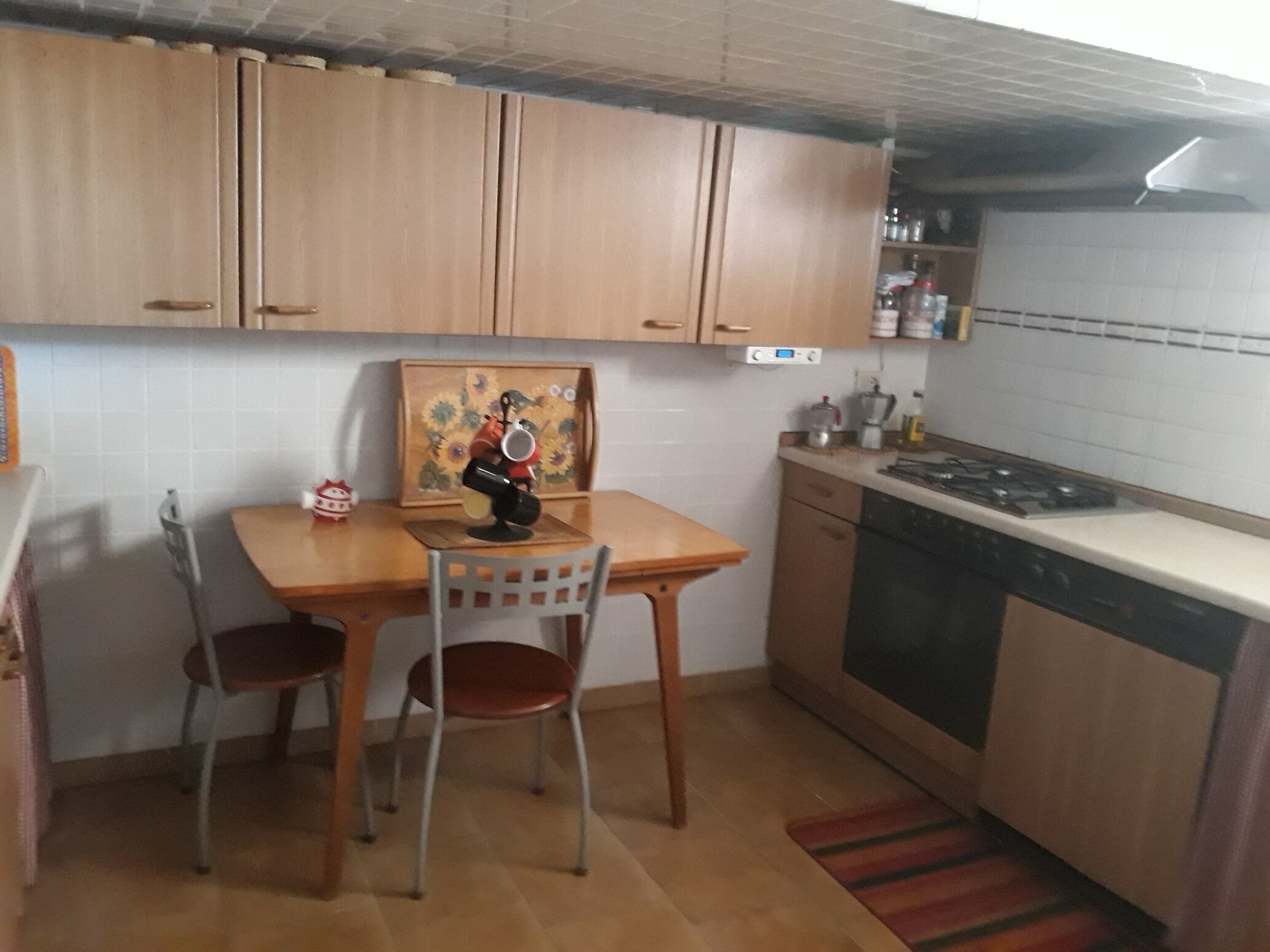 A compact kitchen with wooden cabinets, a dining table with two chairs, a stove, and a small refrigerator.