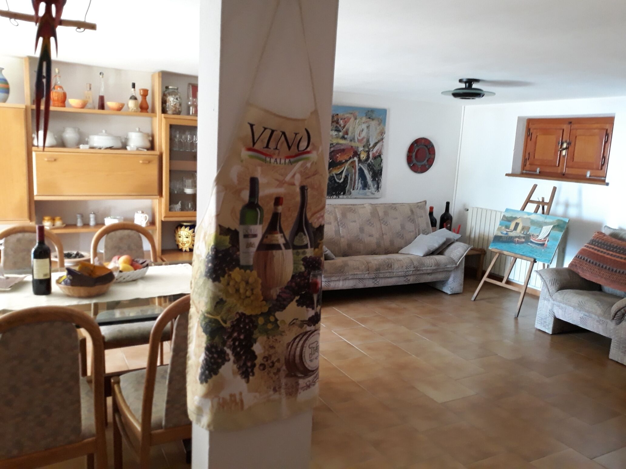 A living room with a sofa, a painting, a wine rack, and a dining area with chairs and a table.