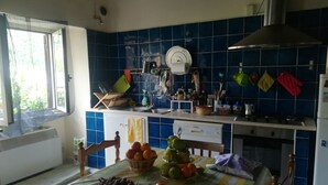 Une cuisine avec des carreaux bleus, une fenêtre, une table avec des fruits et un fourneau.