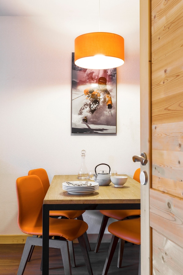 A dining area with a wooden table, orange chairs, a hanging orange lamp, and a framed picture on the wall.