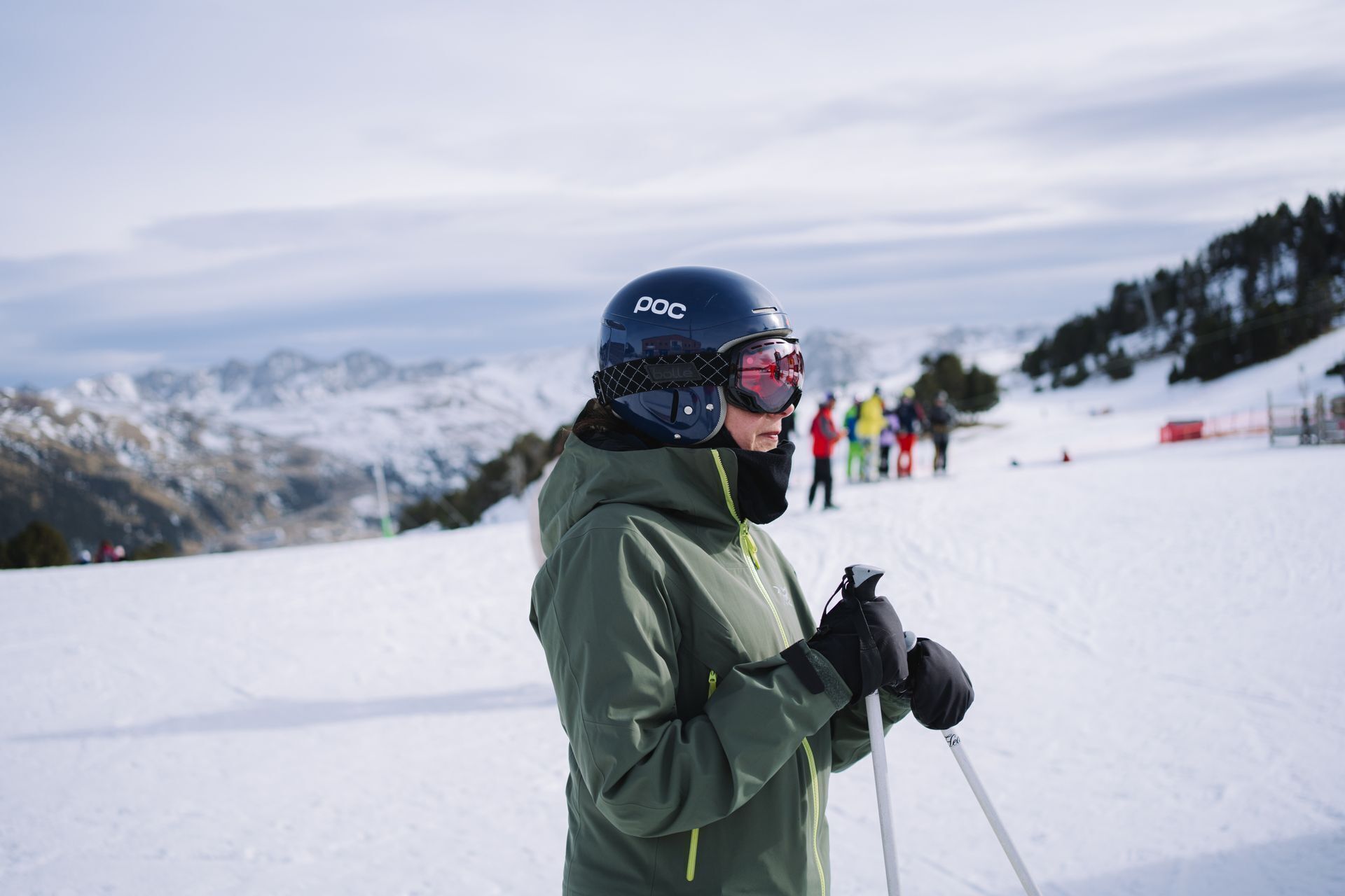 En person som åker skidor i en snötäckt backe, bärande hjälm och skidglasögon, och håller i stavar.