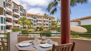 Un comedor con una mesa preparada para dos, con vista a una piscina y un edificio con balcones.