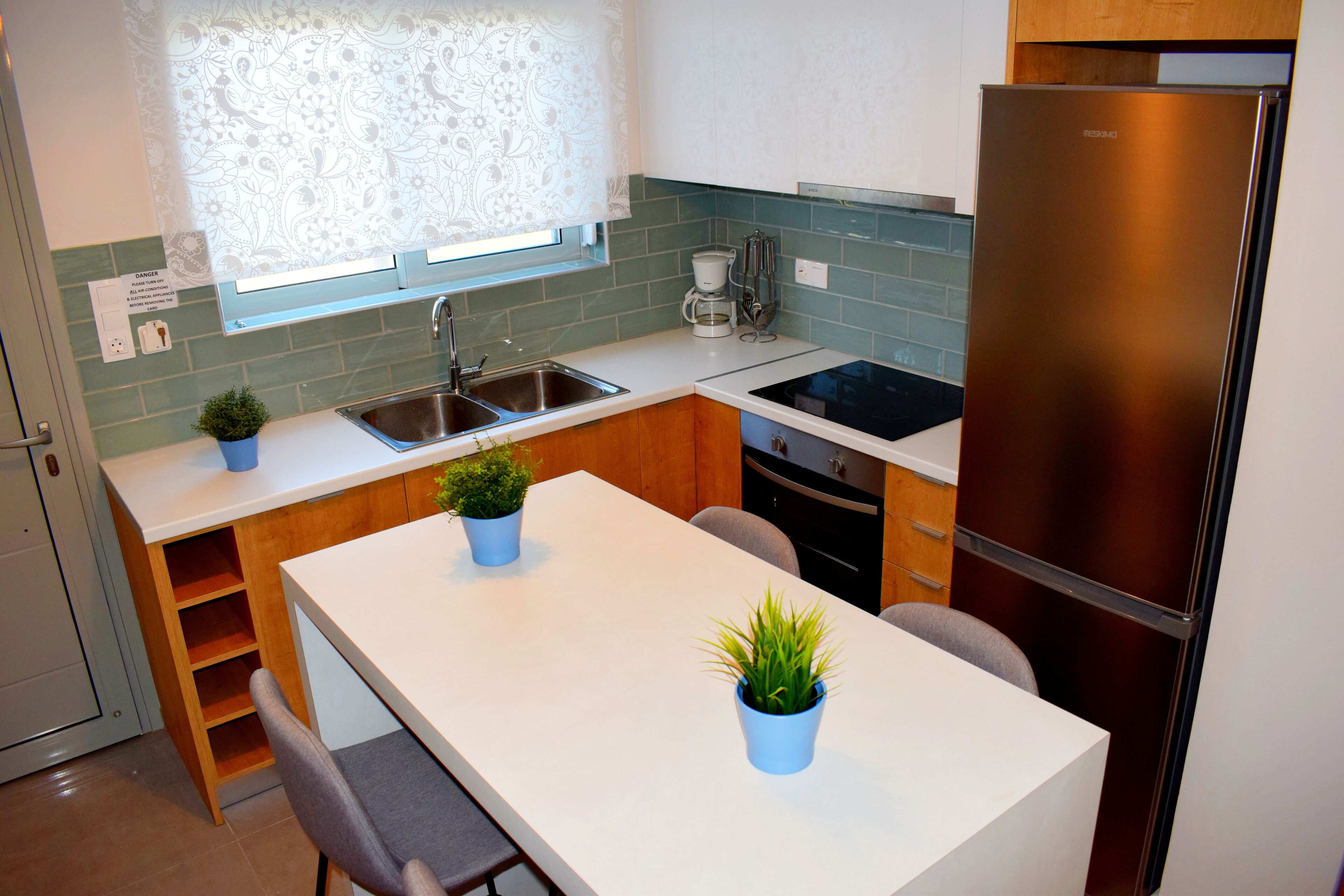 Cocina compacta con refrigerador, lavamanos y ventana con diseño floral.