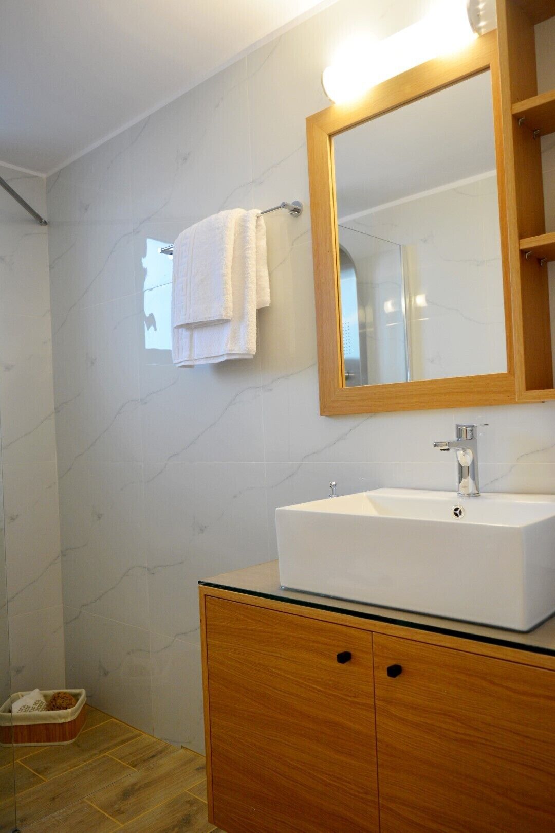 A modern bathroom with a white sink, wooden cabinet, and a large mirror.