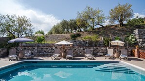 A swimming pool with lounge chairs and umbrellas, surrounded by stone walls and trees. - Private Villa with swimming pool for up to 28 guests (Taormina)