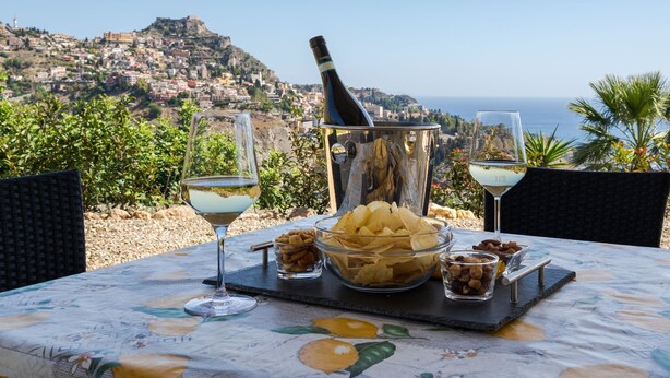 A table with a bottle of champagne, two glasses, and a bowl of snacks, set against a scenic coastal backdrop. - Private Villa with swimming pool for up to 28 guests (Taormina)