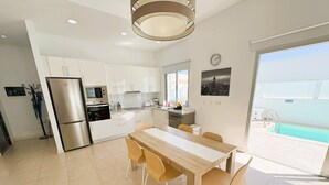 Una cocina moderna con armarios blancos, un refrigerador de acero inoxidable y un comedor con mesa y sillas de madera.