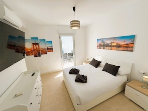 Une chambre d’hôtel équipée d’un lit, d’un bureau, d’une chaise, d’une télévision et décorée avec des œuvres d’art aux murs.