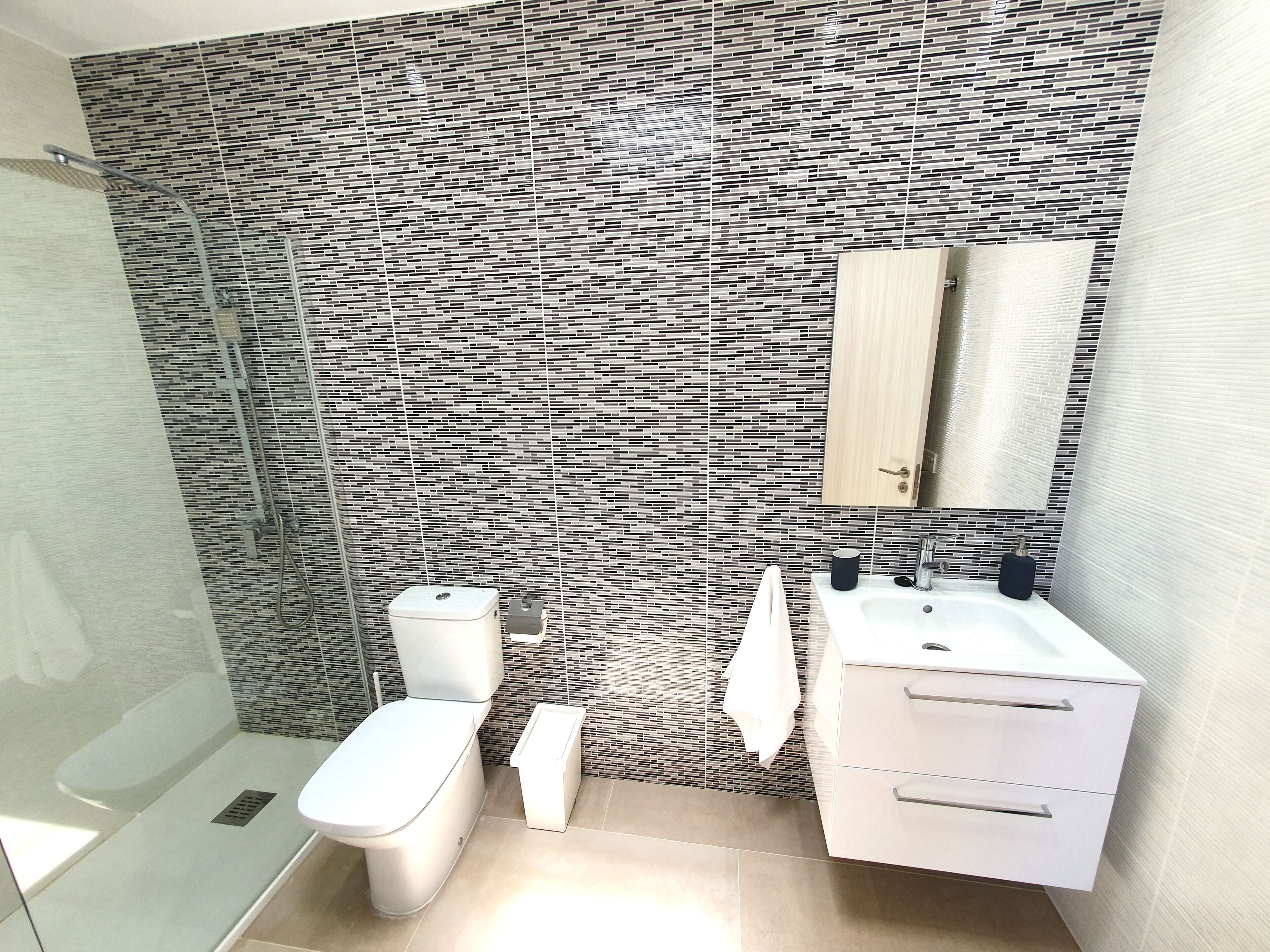 Une salle de bain moderne avec un mur à motifs, des toilettes, un lavabo avec un miroir et un espace douche.