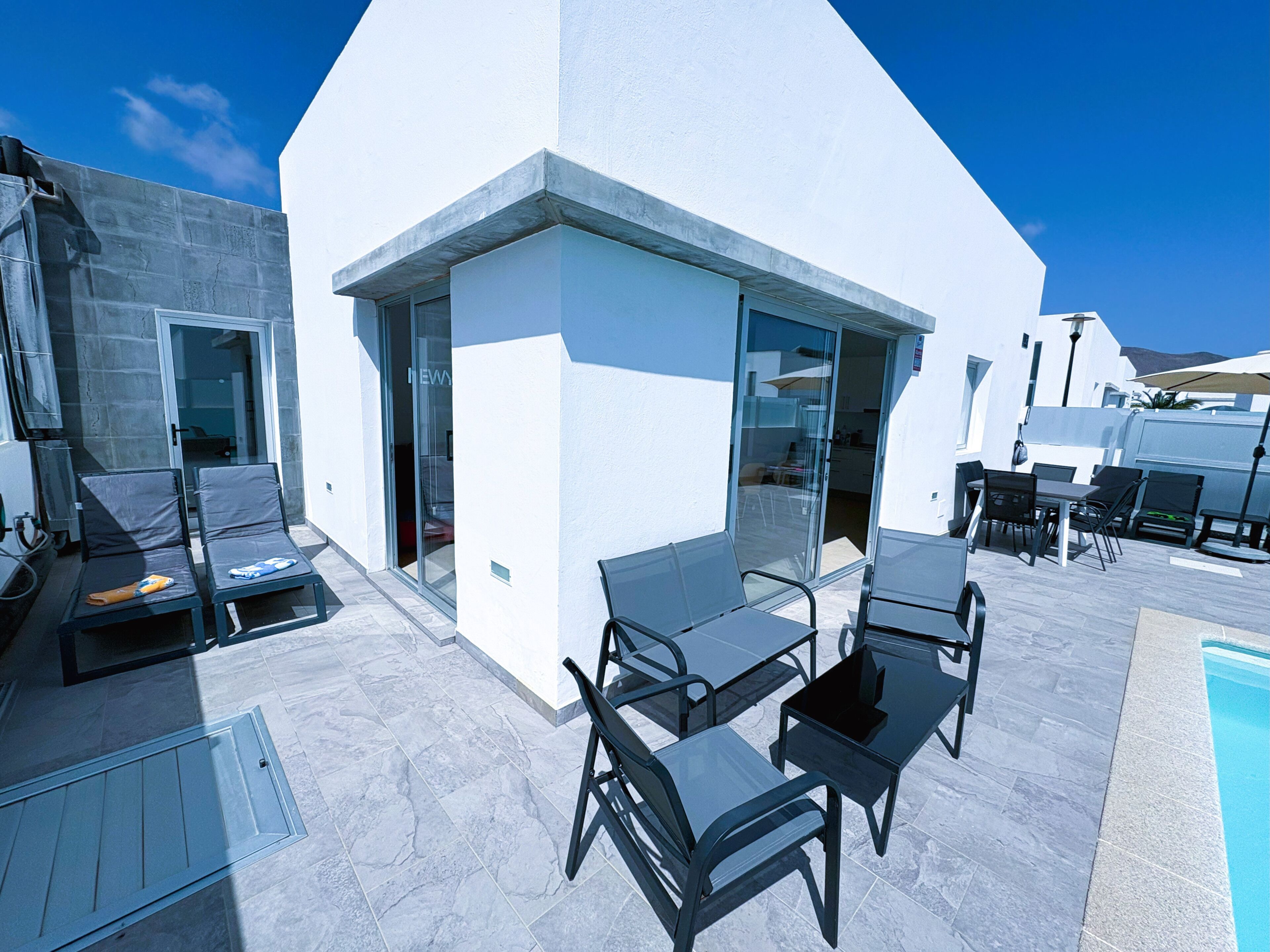 Una moderna terrazza esterna con piscina, sedie a sdraio e zona pranzo.