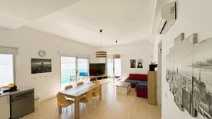Una cocina moderna con comedor, una sala de estar con sofá y un amplio ventanal con vista panorámica de la ciudad.