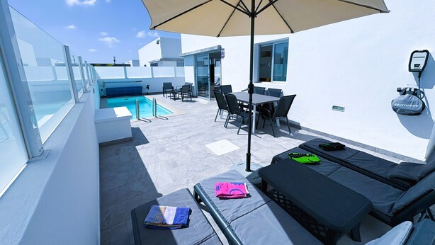 Terraza en la azotea con piscina, mobiliario exterior y una gran sombrilla.