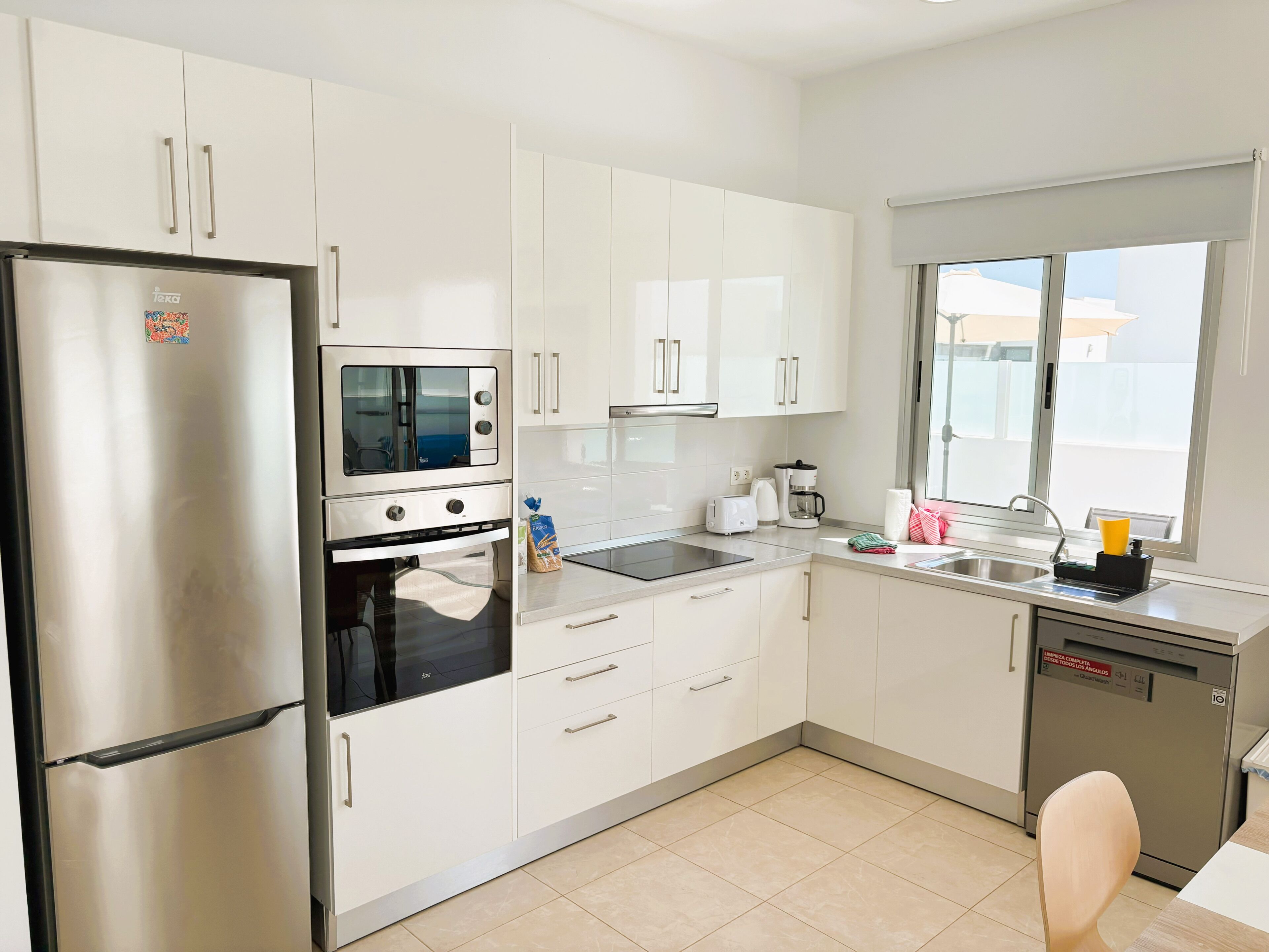 A modern kitchen with white cabinets, a stainless steel refrigerator, an oven, a microwave, a coffee maker, and a dishwasher.