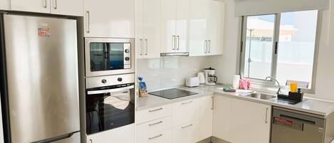 A modern kitchen with white cabinets, a stainless steel refrigerator, an oven, a microwave, a coffee maker, and a dishwasher.