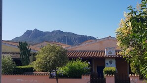 A building with a tiled roof, a cactus, and a mountain in the background. - Home description (Viddalba)