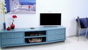 A living room with a blue entertainment unit, a flat-screen TV, a painting of a coastal scene, and a vase with flowers.