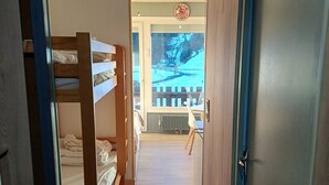 Un couloir étroit, avec des lits superposés d’un côté et une porte de l’autre.