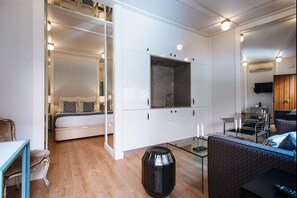 A modern bedroom with a glass partition, a bed, a small table, and a seating area with a sofa and chairs. - Hommyhome Regina (Sevilla)